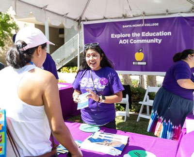 a woman in a purple shirt working at an outdoor booth 
