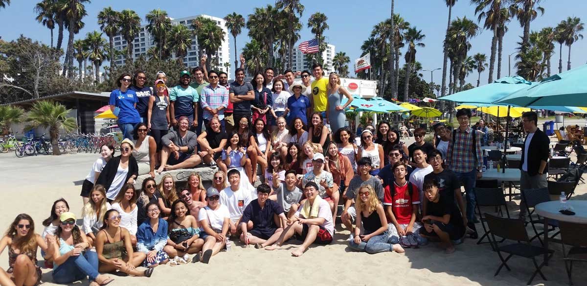large group of smiling students pose for a photo at the beach