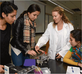 An instructor in a white coat and three female students