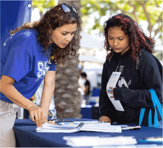 two women look at papers on an outdoor table